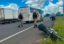 Acidente entre moto e transporte coletivo termina em morte em Uberlândia Local do acidente isolado com fita zebrada, mostrando a motocicleta caída no asfalto próxima a um ônibus urbano e policiais militares ao fundo
