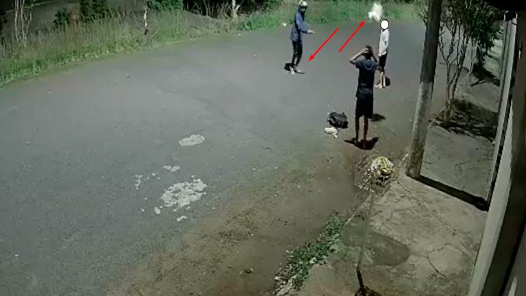 Captura de tela de câmera de segurança mostrando um assaltante de capacete chutando um buquê de flores no chão enquanto vítimas se afastam