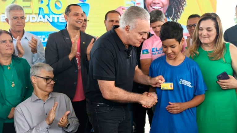 Estudante segurando um celular com o aplicativo Ubetrans aberto em frente a um ônibus do transporte público de Uberlândia