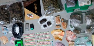 PM apreende drogas após fuga de suspeitos no Residencial Integração Diversos tipos de drogas, comprimidos de ecstasy, balanças de precisão e dinheiro espalhados sobre uma mesa de delegacia