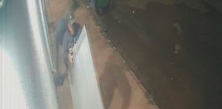 Até a porta: Ação de criminosos surpreende moradores do bairro Morumbi Imagem de câmera de segurança mostrando um homem de casaco escuro carregando uma porta de alumínio branca em uma rua à noite.