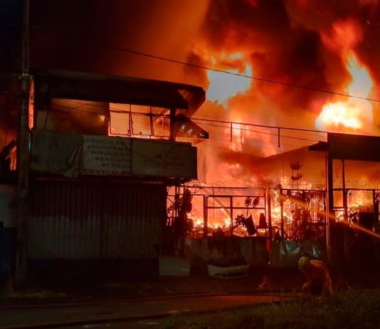 Bombeiros combatem incêndio em ferro-velho de Uberlândia; fogo atingiu casa e carro Bombeiros combatendo chamas altas em um ferro-velho à noite em Uberlândia.