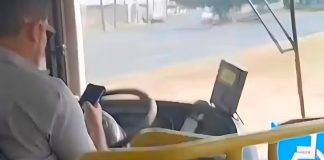 Passageiro filma motorista de ônibus soltando o volante para usar celular no Triângulo Mineiro Foto de interior de ônibus mostrando o motorista segurando um celular enquanto conduz o veículo.