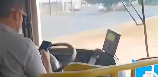 Passageiro filma motorista de ônibus soltando o volante para usar celular no Triângulo Mineiro Foto de interior de ônibus mostrando o motorista segurando um celular enquanto conduz o veículo.