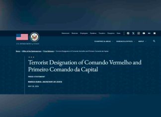 Facções brasileiras PCC e CV entram para a lista de terroristas globais dos EUA Bandeira dos Estados Unidos em primeiro plano com o prédio do Departamento de Estado americano ao fundo em Washington.